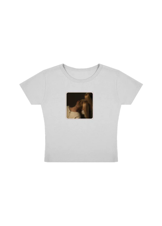 White cropped Ariana Grande t-shirt featuring a centered square photo of two women leaning in close, bathed in warm lighting. A minimal, intimate design celebrating the emotional tone of the eternal sunshine era.