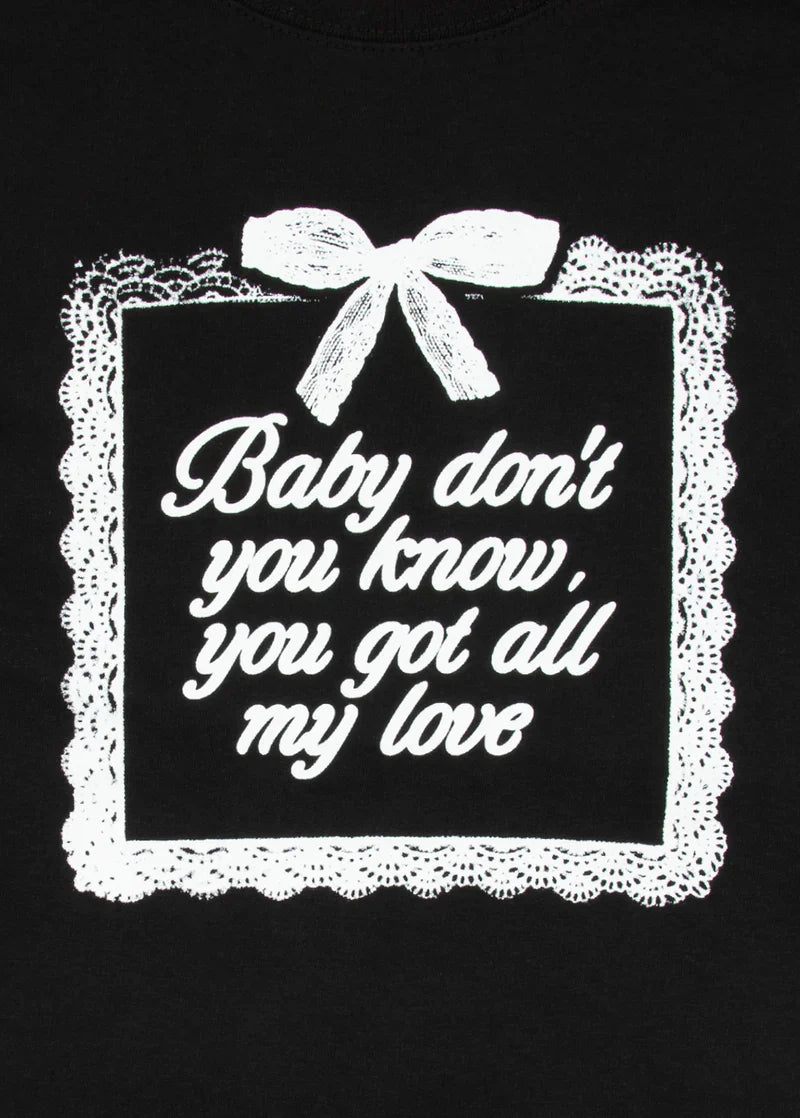 Close-up of white text reading 'Baby don’t you know, you got all my love' inside a delicate lace-trimmed frame with a bow, printed on black fabric. Soft romantic visuals meet iconic Ariana Grande lyrics.
