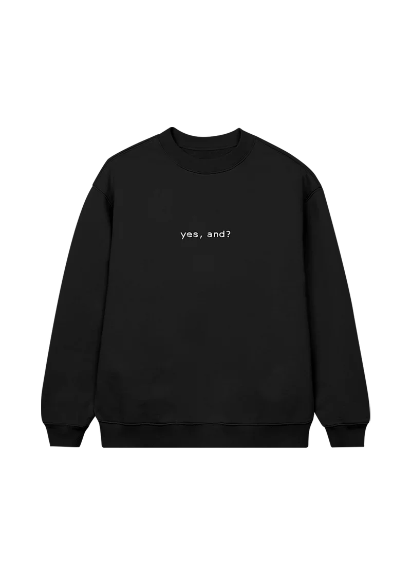 Black Ariana Grande crewneck sweatshirt with minimalist white text that reads “yes, and?” centered on the front — a statement piece from the official merch line.