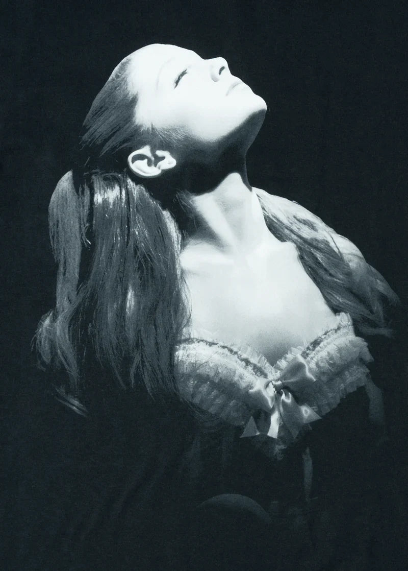 Close-up of grayscale photo print on black t-shirt, showing Ariana Grande in a vintage-inspired lace corset top, dramatically lit with her head tilted upward. A standout visual from the Yours Truly album re-release.