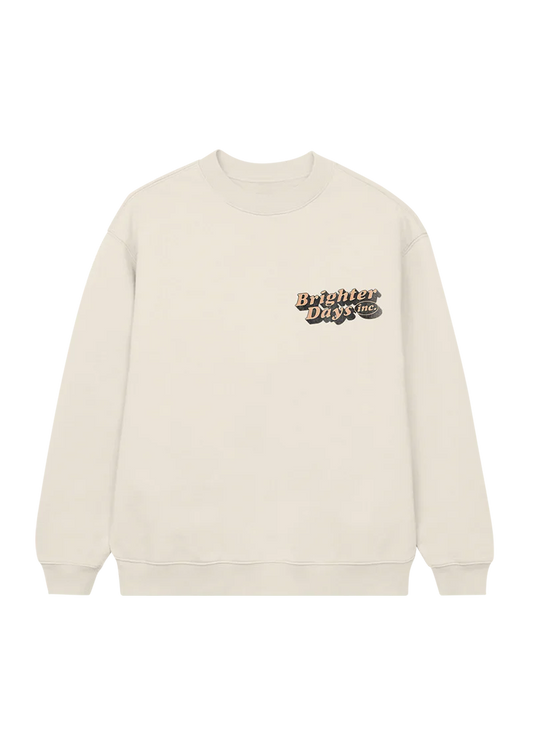 Cream crewneck sweatshirt with a small retro-style “Brighter Days Inc.” logo printed on the left chest in bold orange and black lettering — cozy and vintage-inspired merch from Ariana Grande’s collection.