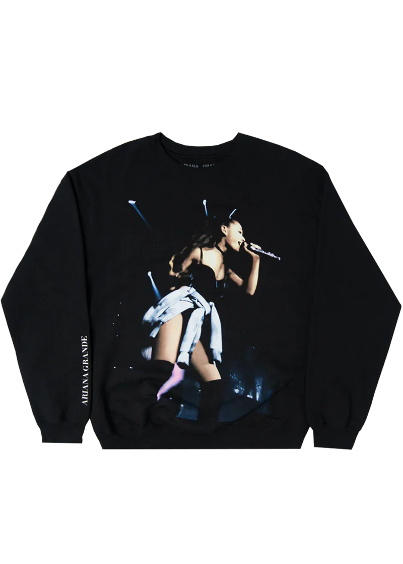Black Ariana Grande crewneck sweatshirt featuring a full-color concert photo from the My Everything tour, showing Ariana mid-performance in cat ears and thigh-high boots, with "Ariana Grande" printed vertically on the sleeve.

