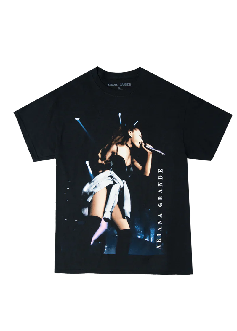 Black Ariana Grande t-shirt featuring a live concert photo from the My Everything era, with Ariana performing on stage in a black outfit and knee-high boots, “Ariana Grande” printed vertically along the side.


