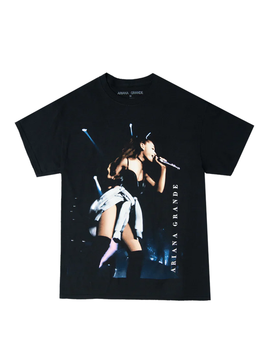 Black Ariana Grande t-shirt featuring a live concert photo from the My Everything era, with Ariana performing on stage in a black outfit and knee-high boots, “Ariana Grande” printed vertically along the side.

