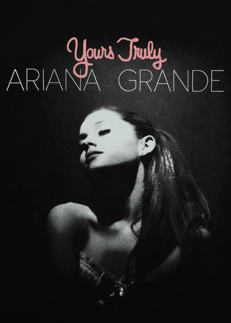 Close-up of puff print design on black tee showing Ariana Grande in spotlight with 'Yours Truly' in pink script and 'Ariana Grande' in white text. Textured print adds a tactile pop.