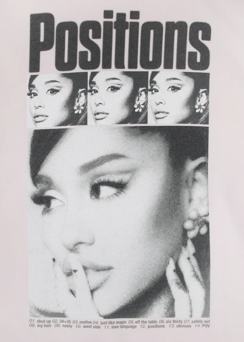 Close-up of the “Positions” crewneck design showing Ariana Grande's portrait, tracklist text, and bold album title — fine print includes all 14 songs from the Positions album.

