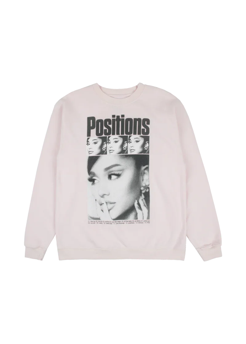 Light pink crewneck sweatshirt featuring a collage-style black-and-white print of Ariana Grande’s face repeated above the bold “Positions” title, with the full tracklist from the album printed beneath.

