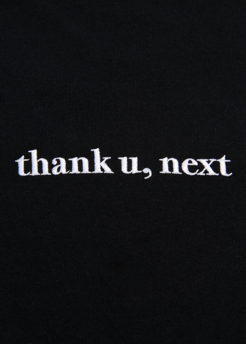 Close-up of the chest embroidery on the Ariana Grande long sleeve t-shirt, showcasing the “thank u, next” text in clean white lettering. A crisp, high-quality detail that elevates this fan-favorite merch.

